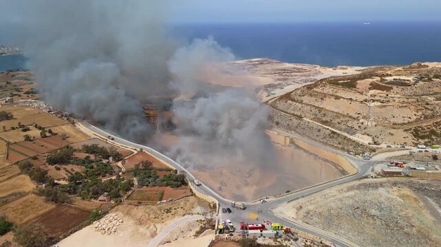 In Maghtab, Malta, an active landfill fire sends thick toxic smoke over the waste site as firefighters and emergency vehicles respond on the ground in an aerial view on May 6th, 2026.