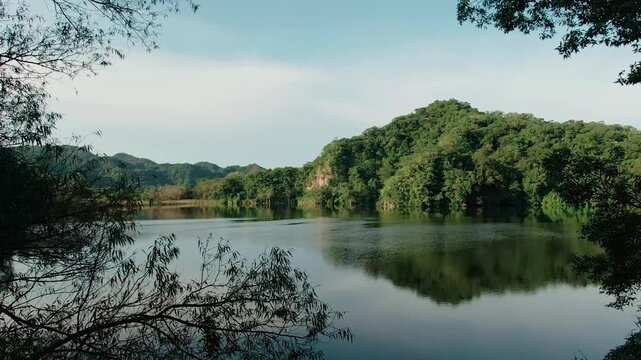 Calm reflective Laguna La Maria volcanic lake bordered by dense tropical forest and green hills in Colima, Mexico