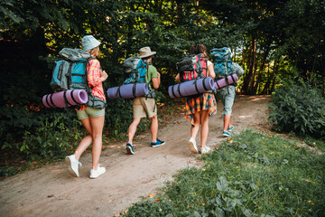 Obraz premium Group of friends hiking through a forest trail with backpacks and sleeping mats on a summer camping adventure