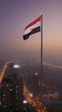 The Iranian flag waves proudly in the breeze against a backdrop of mountains and a cityscape at sunset