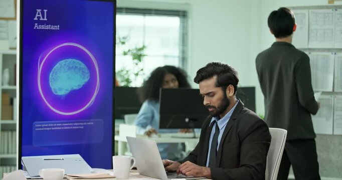 Mixed race Businessman, programmer working on a computer while looking at AI assistant interface on monitor at office. Smart workplace automation, future software engineering, machine learning concept