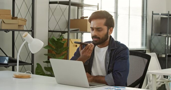 Businessman using a voice command features talking to a virtual AI assistant while working on a laptop at office. Speech recognition, Smart business entrepreneur technology and mobile automation.