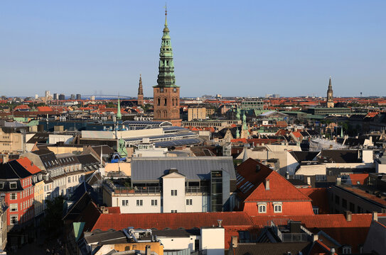 Panoramic aerial view of the city center of Copenhagen (Denmark) with views of the many spires, the Vor Frelsers Kirke church and the Oresundsbroen bridge in the background aginst a clear blue sky