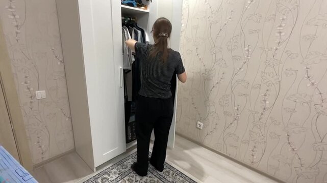 Selecting attire for day. Morning dressing with careful outfit choice. Woman meticulously chooses her clothing in closet. Diligently planning her outfit as she selects jacket from her wardrobe