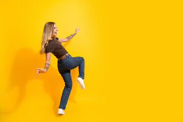 Obraz premium Joyful young woman dancing on bright yellow background in jeans and sneakers, casual lifestyle pose showing motion, happiness and fashion energy