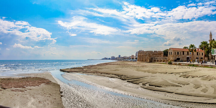 Panoramic coastal view of Finikoudes beach and medieval castle fort in Larnaca. Beautiful mediterranean landscape with sea shore, stone fortress, historic  minaret and palm under blue sky. Cyprus