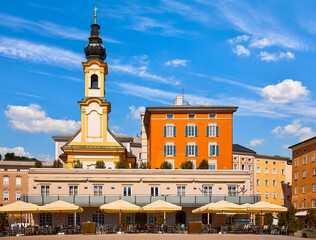 Obraz premium Salzburg, Austria. Chapel tower and street cafe of the central square of the historic old town among old austrian buildings architecture. Sunny summer day. Blue sky with clouds.