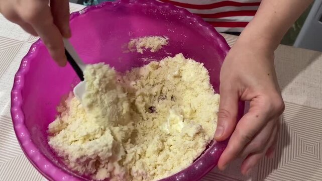 caucasian recipe creator stirring crumbly mixture with spatula in bright pink bowl, coarse grainy texture folding into moist pockets, focused hands and casual kitchen setup, home baking tutorial