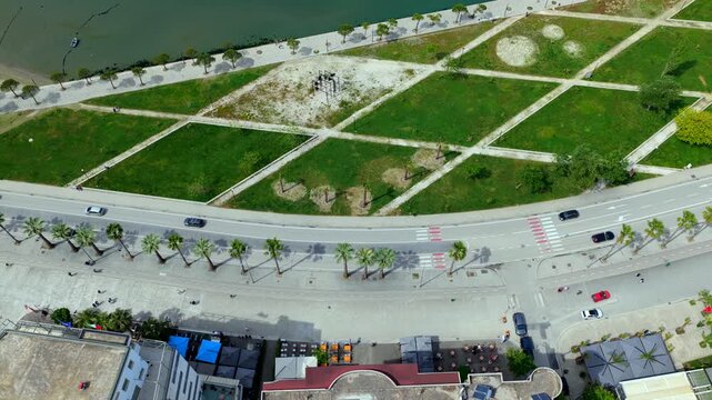 Aerial video over the coastal avenue of Vlora, Albania, featuring modern apartment rooftops, a palm lined boulevard with moving traffic