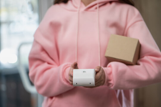 A close-up of a girl delivering parcels, a courier with a box and a wireless payment terminal, unrecognizable