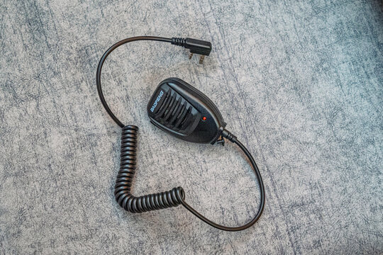 Baofeng PTT with cable and dual plug connection under grey fabric surface.