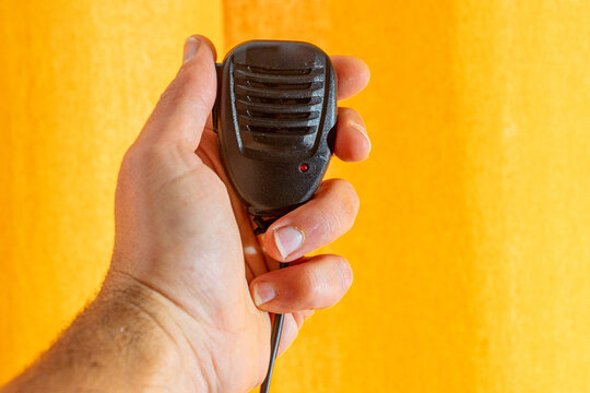 PTT, secure microphone in white man's hand on yellow fabric surface in backlight.