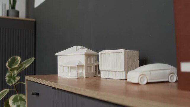 Close up no people shot of detailed plastic models of residential building, modern cubic structure, and streamlined car model, created using 3D printer