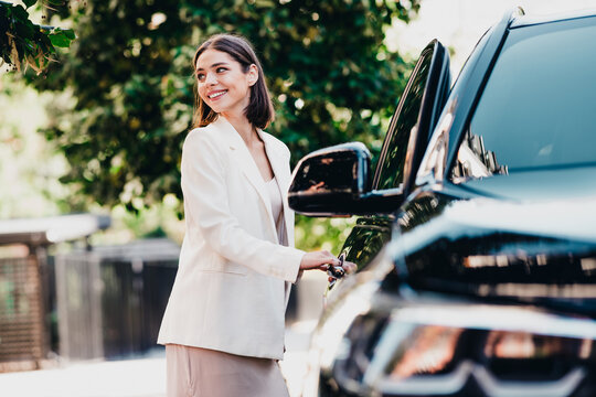 Smiling businesswoman opening a car door in an urban setting, dressed in a white blazer and skirt conveying confidence, professionalism and modern commuting lifestyle