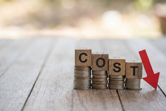 Wooden blocks spelling COST on coin stacks with a red arrow pointing down, symbolizing cost reduction and financial savings.