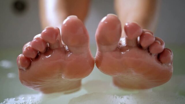 Flexing bare feet pressing then parting in tub, shifting foam into bubbles, showing wet soles
