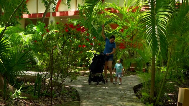 A young mom and her baby exploring a beautiful tropical museum garden. They look up with wonder at a magnificent giant Ceiba tree, enjoying nature and family time.