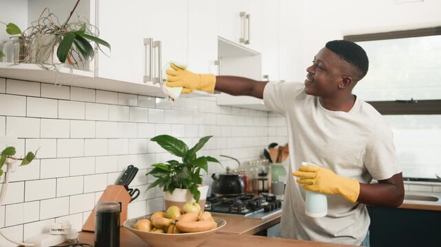 Young Man Cleaning Kitchen Cabinets With A Spray Bottle And Cloth At Home