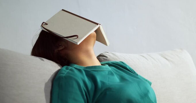 A woman enjoys a light-hearted nap with a book resting her face showcasing a cozy moment.