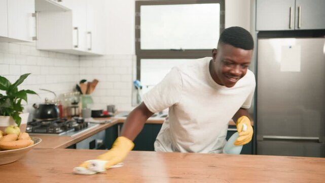 Happy African American Man Cleaning Modern Kitchen Countertop with Spray and Cloth