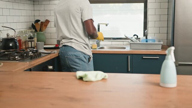 Man In Yellow Gloves Washing Dishes In A Bright, Modern Kitchen After A Meal