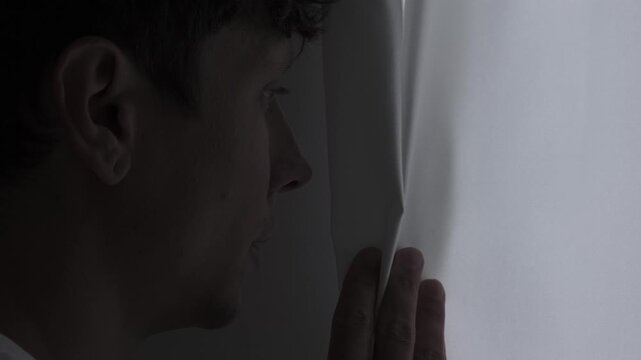 Paranoia and anxiety concept with suspicious person carefully looking through curtain, psychological fear, stress and unsafe feeling atmosphere, close-up