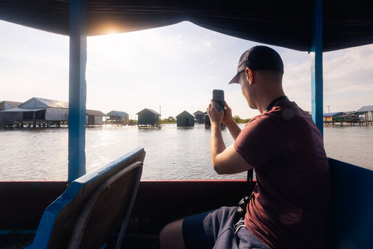 Tourist in boat taking photo with mobile phone of floating village on Tonle Sap lake Cambodia. Exploration, travel photography, tourism, and asian vacation concept.