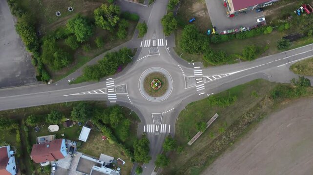 Aerial view rotating over a roundabout in Dambach-La-Ville, France, with cars circulating through. Top-down perspective drone shot, during a summer evening.