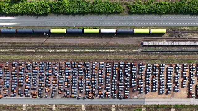 Aerial top down view of a freight train with colorful wagons traveling along a railway line next to a steel coil warehouse, showcasing industrial logistics and transportation concepts