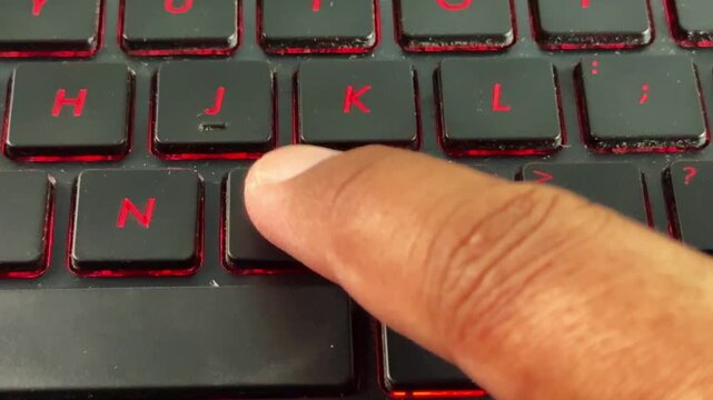 Close-up of keyboard typing with red backlight on "M" button, suitable for cybersecurity, programming, and tech content.