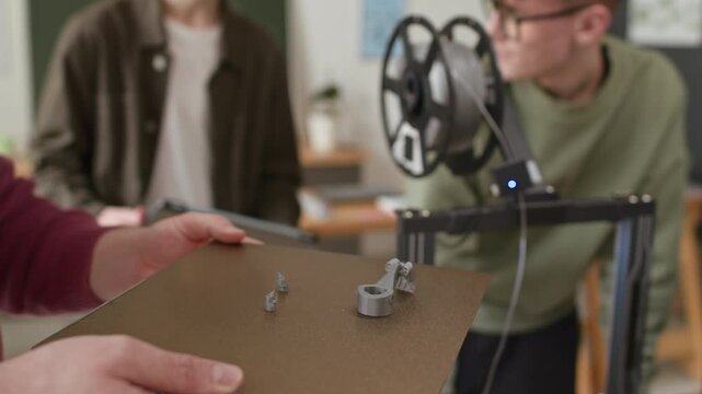 Close up shot of unrecognizable teacher demonstrating result of 3D printing of gray plastic part on flexible base and preparing to remove it for closer examination during class
