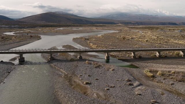 Bridge crosses R&iacute;o Grande near Bardas Blancas along National Route 145 in Paso Pehuenche, Mendoza Cuyo Argentina, within the Andes foothills, drone orbit aerial shot above braided river channels.