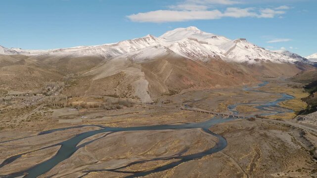 R&iacute;o Grande meanders through braided Andean valleys near Bardas Blancas and Route 40 in Mendoza Province, Cuyo Region, Argentina, slow forward flyover aerial shot above snowy mountain terrain.