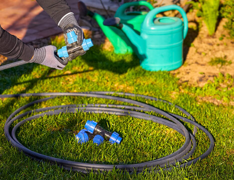 Closeup of hands in the gloves. Process of plumbing, installing fittings pipes and connectors for the garden and lawn irrigation system installation. Green grass, shallow depth of field.