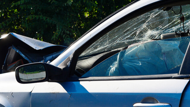 Silver passenger car after a traffic collision on a city street. Damaged automobile with crushed bodywork and broken parts left outdoors on a public road after a vehicle accident or crash.