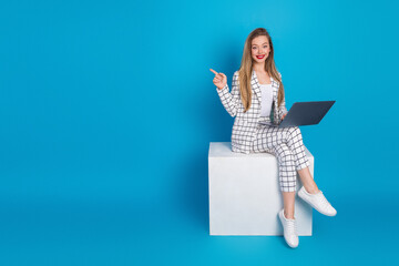 Naklejka premium Smiling businesswoman with laptop pointing to space for text on blue background, casual modern professional portrait