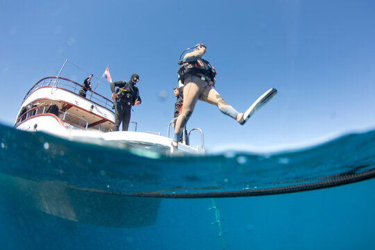 Group of divers jumping into water from a boat under clear blue sky in daylight