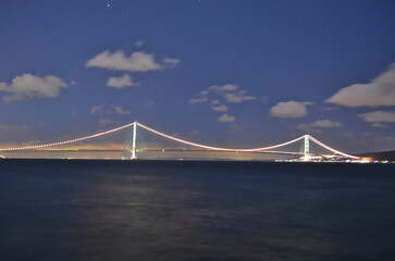 Obraz premium KOBE, JAPAN - FEBRUARY 12, 2023: Beautiful night illumination of the Akashi Kaikyo Bridge glowing in the dark against the night sky