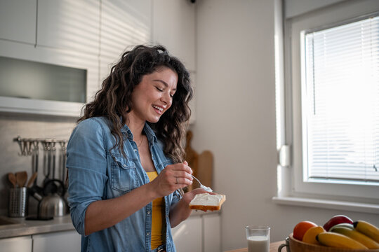 Happy woman spreading cream cheese on toast for breakfast
