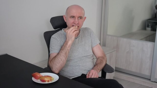 Bald man eating fresh apple slices while relaxing on sofa at home video HD Full
