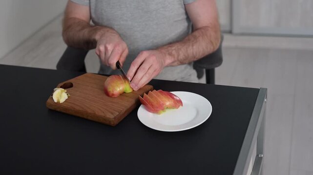 Bald man slicing red apple into pieces on wooden cutting board at home Full HD video