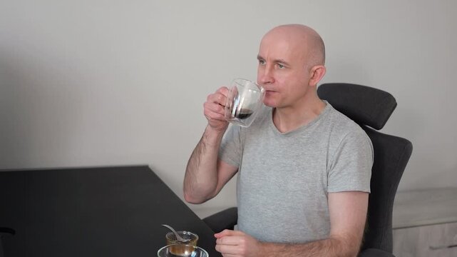 Bald man eating cookies and drinking hot beverage while sitting at home kitchen video table Full HD