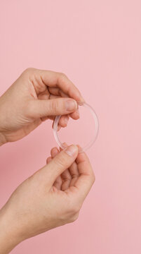 emale hands holding a clear flexible vaginal contraceptive ring against a pastel pink background. Women's health, safe sex, family planning and sexual education concept