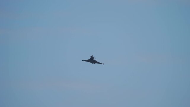 Delta wing canard fighter jet captured from directly below showing full wing planform, aircraft banking against a pale grey-blue sky