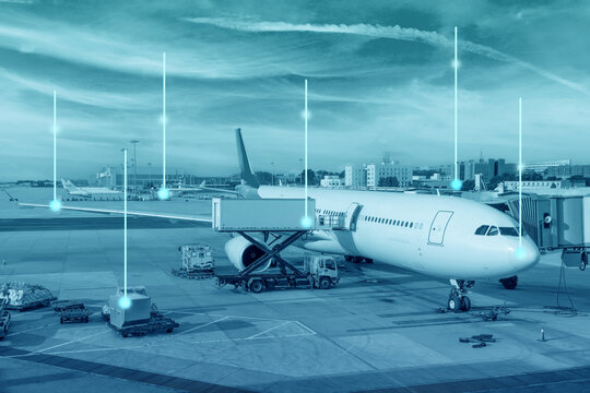 Passenger aircraft receives cargo loading by ground vehicles at an active airport tarmac, with glowing digital lines showing data connectivity during daytime