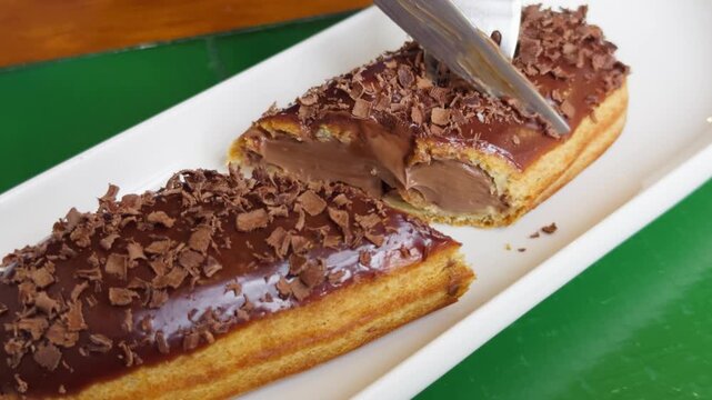 Fresh sweet eclair cake with cream cheese and chocolate chips on the table in a cozy cafe. High quality 4k footage