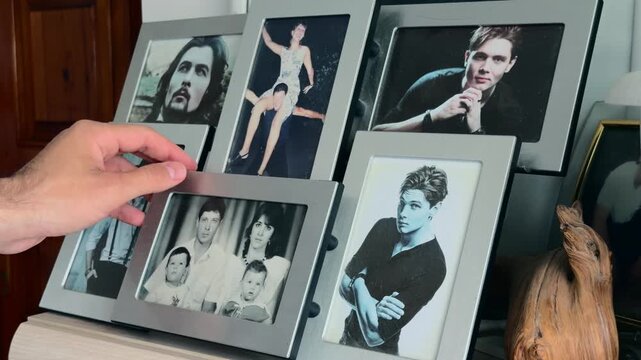 Close up of an unrecognizable male hand gently touching and stroking silver frames with old family portrait photos conveying nostalgia memories and generational heritage in soft natural indoor light.