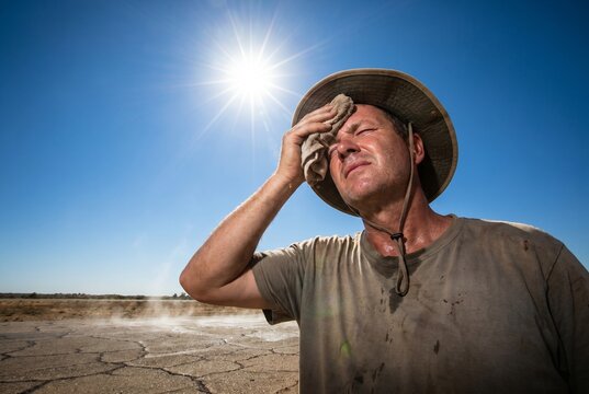 Homme &eacute;puis&eacute; essuyant la sueur de son front sous un soleil br&ucirc;lant, concept de canicule, de s&eacute;cheresse extr&ecirc;me et d'insolation