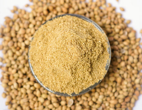 A glass pot filled with organic Coriander powder, placed over a head of whole coriander seeds on white background. Indian spices Coriander or Dhaniya powder , ingredient for Indian cooking.