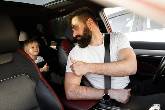 Father driver showing thumbs up sign to his little son in safety car seat. Happy dad and toddler boy smiling in vehicle interior before trip. Family road travel, male driver buckle up seatbelt